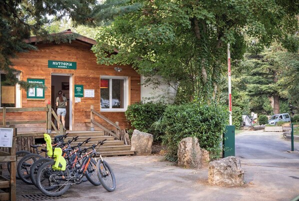 A wooden cabin labeled "Huttopia Accueil" with bicycles parked outside, surrounded by trees and rocks. - Huttopia Millau (Millau)