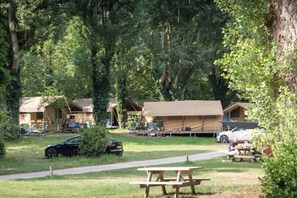 A campsite with tents, picnic tables, and a car parked on the grass. - Huttopia Millau (Millau)