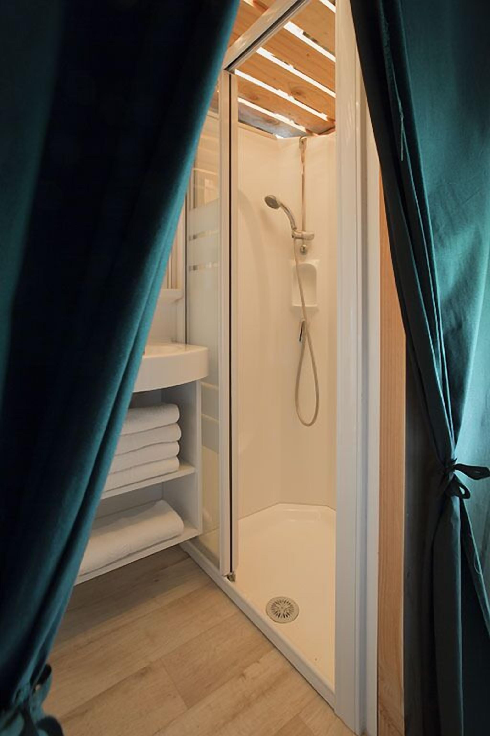 A shower area with a glass door, a towel rack, and a shelf with folded towels.