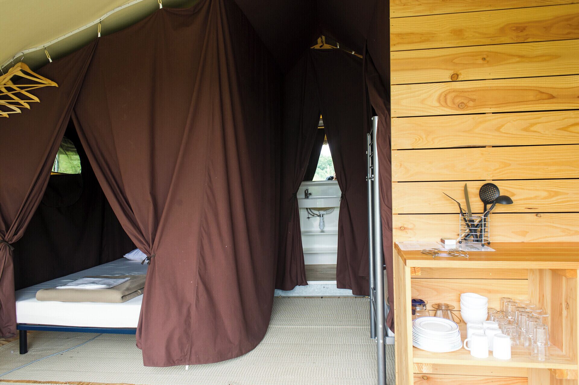 A tent with a bed, a sink, and a shelf with dishes and utensils.