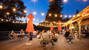 Un área de comedor al aire libre con luces colgantes y mesas y sillas de madera.