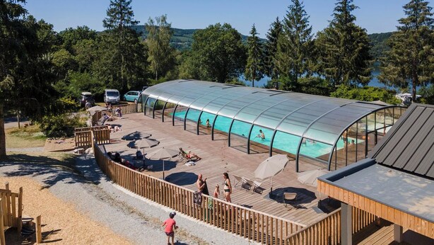Una piscina cubierta con solárium de madera, sillones de descanso y sombrillas.
