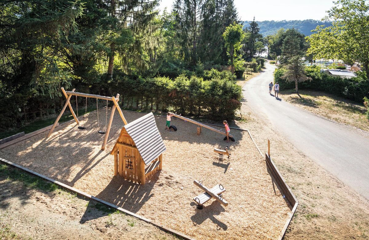 Une aire de jeux avec une maison en bois, une balançoire et des balançoires classiques.