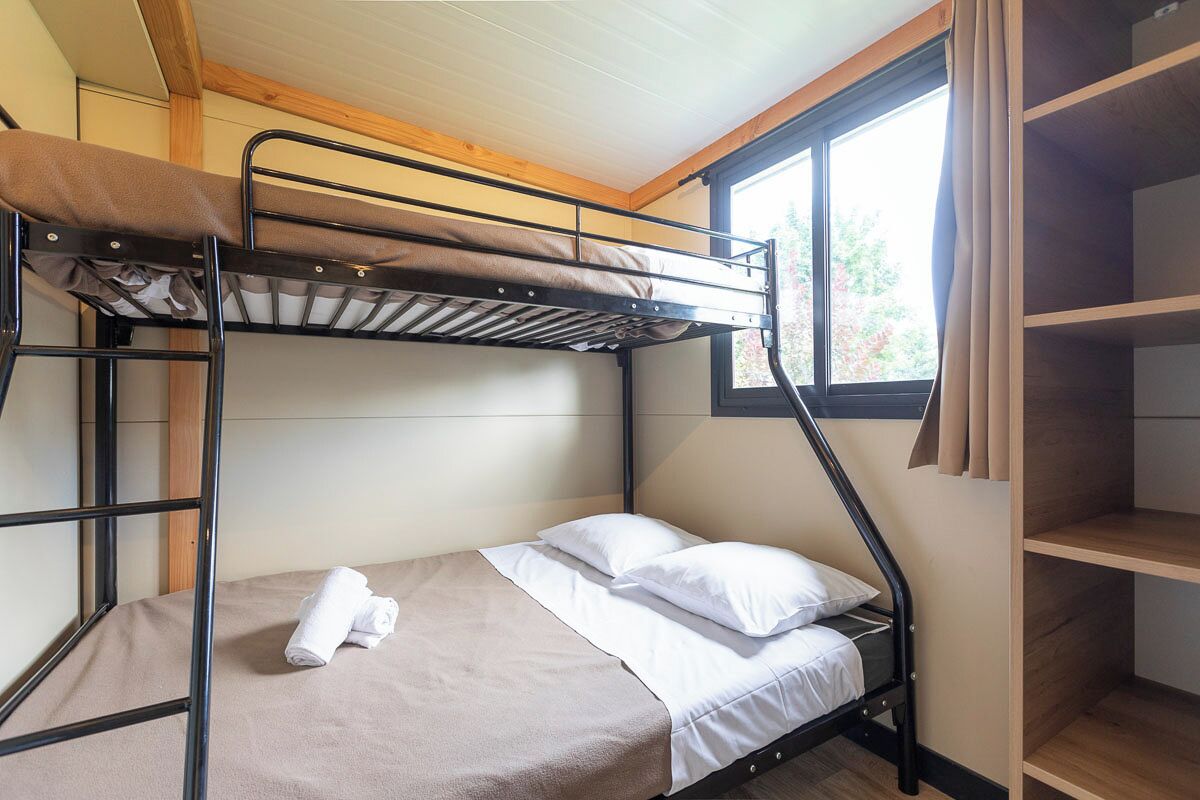 A bunk bed room with a window, a wooden ceiling, and a shelf unit.