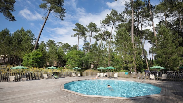 A swimming pool with a wooden deck, surrounded by trees and equipped with lounge chairs and umbrellas. - Huttopia Landes Sud (Saint-Michel-Escalus)