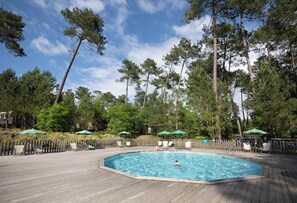 Una piscina con cubierta de madera, rodeada de árboles y equipada con sillas de descanso y sombrillas.