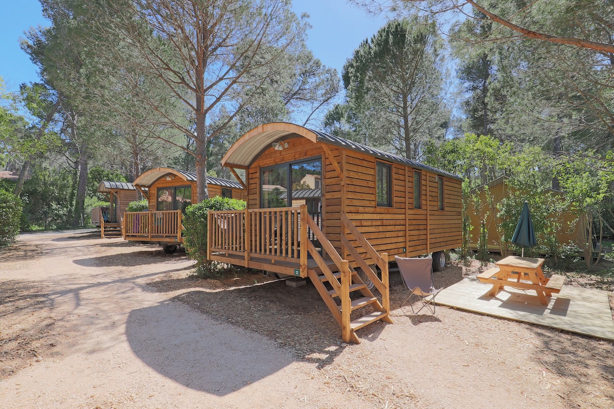 Une cabane en bois dotée d’une terrasse et d’un escalier, entourée d’arbres.