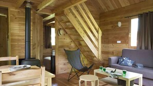 A cozy cabin interior with a wooden interior, a sofa, a dining table, and a chair. - Huttopia Lac de Rillé (Rillé)