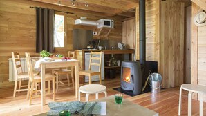 A cozy wooden cabin with a dining area, a kitchen with a stove, and a large window. - Huttopia Lac de Rillé (Rillé)