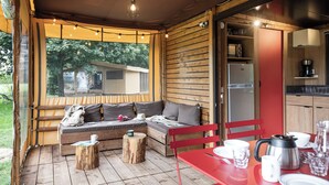 Ein gemütliches Blockhaus mit Holzvertäfelung, einem Essbereich mit rotem Tisch sowie einer Sitzecke mit Sofa und Kissen.