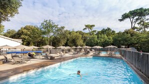 Ein Schwimmbecken mit Liegestühlen und Sonnenschirmen, umgeben von Bäumen.