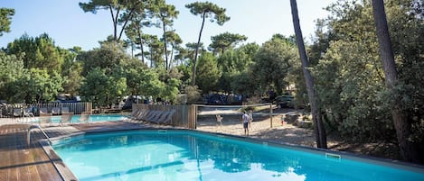En swimmingpool med ett trädäck, omgiven av träd och ett inhägnat område med solstolar.