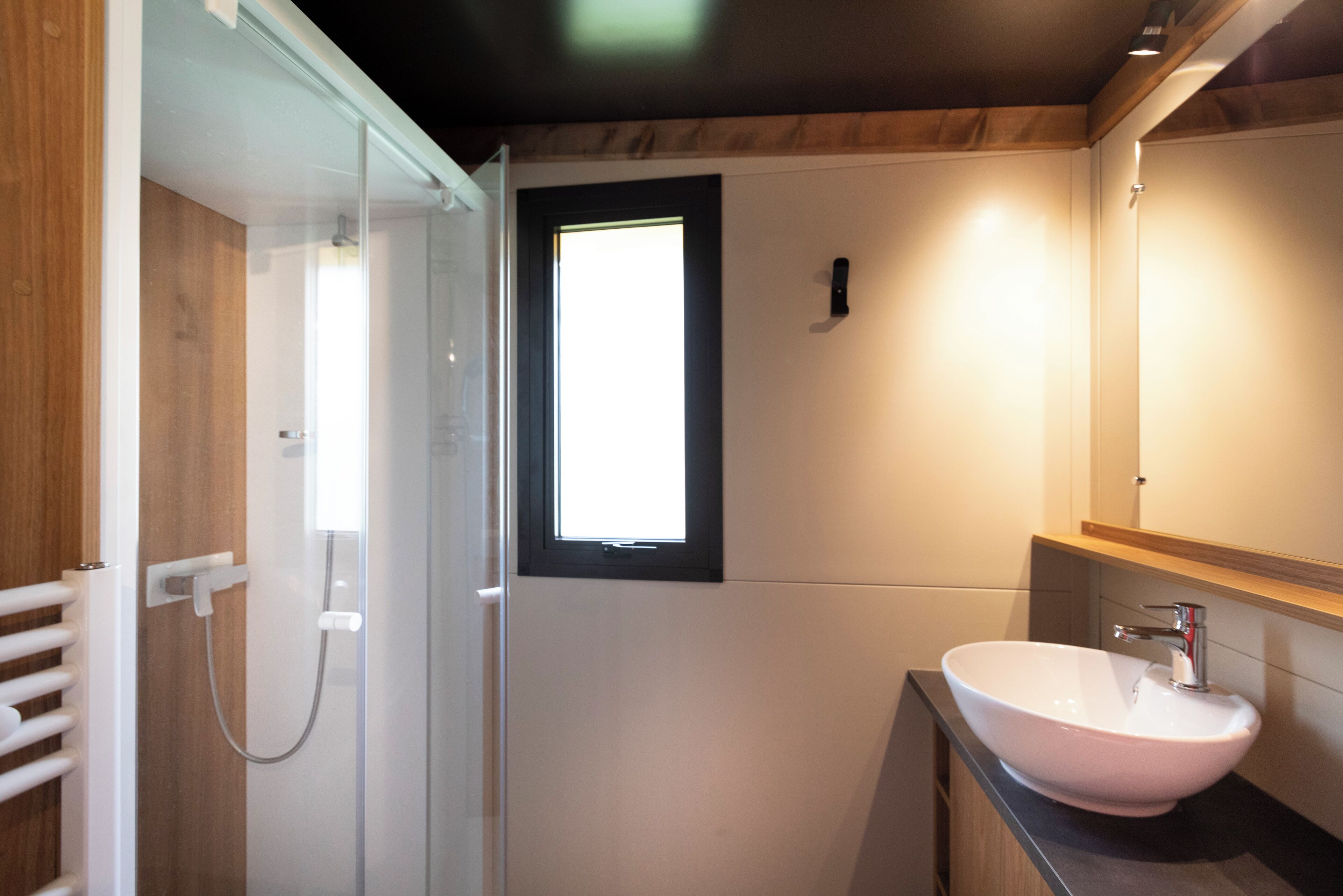 A modern bathroom with a glass shower enclosure, a white sink, and a wooden vanity.