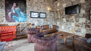 Una habitación con paredes de piedra, un cuadro grande, una mesa de centro de madera, sofás de cuero y una silla roja.