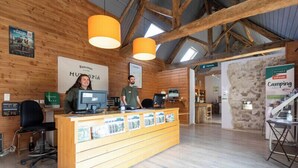 Un mostrador de recepción de madera con una computadora y folletos, una pared de piedra y un letrero para camping.
