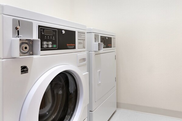 A front view of a commercial washer and dryer unit with a control panel, a water inlet, and a door handle.