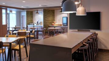 A modern dining area with multiple tables and chairs, a long counter with stools, and pendant lighting.