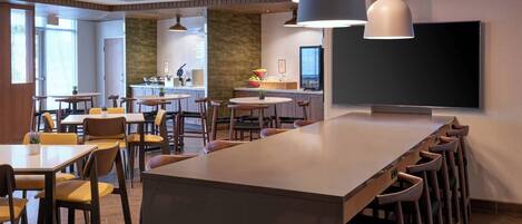 A modern dining area with multiple tables and chairs, a long counter with stools, and pendant lighting.