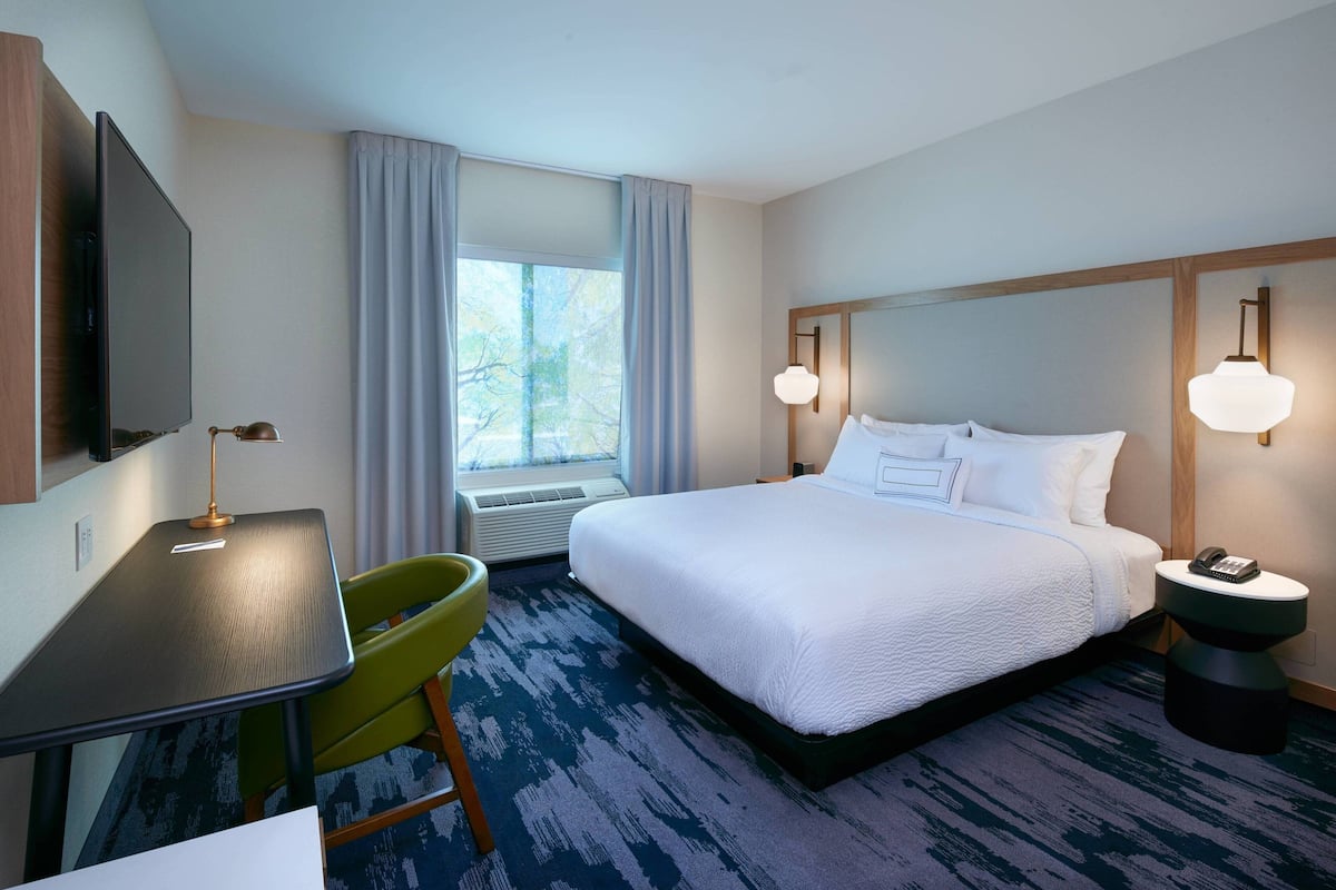 A hotel room with a bed, a desk, a chair, a TV, and a window with curtains.