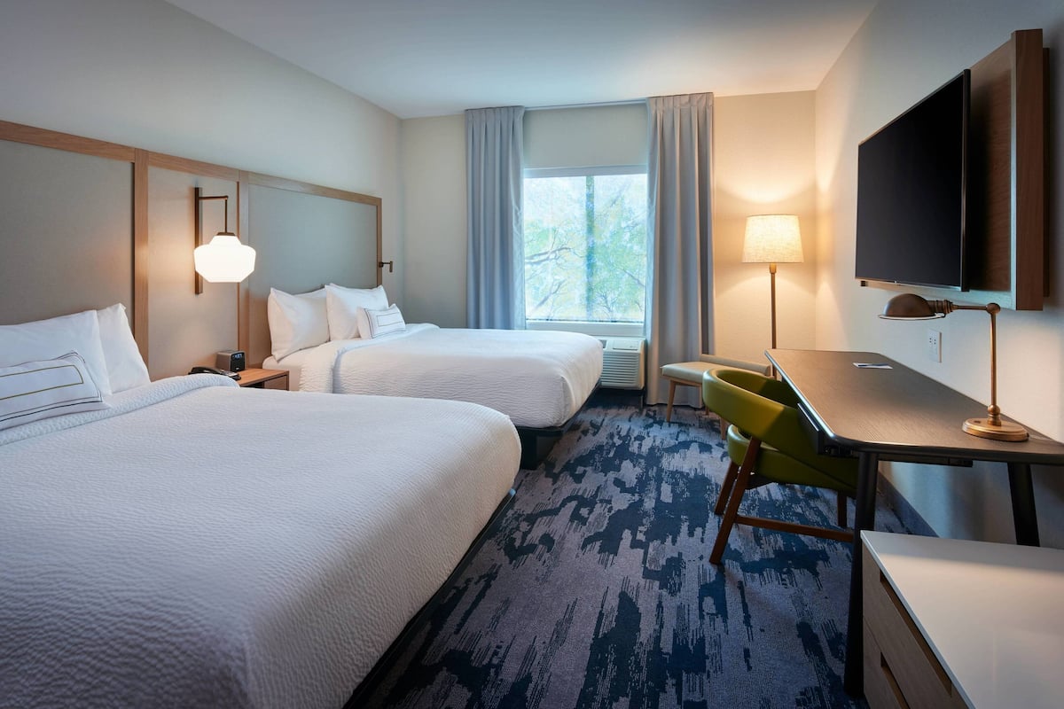 A hotel room with two beds, a desk, a chair, a TV, and a window with curtains.