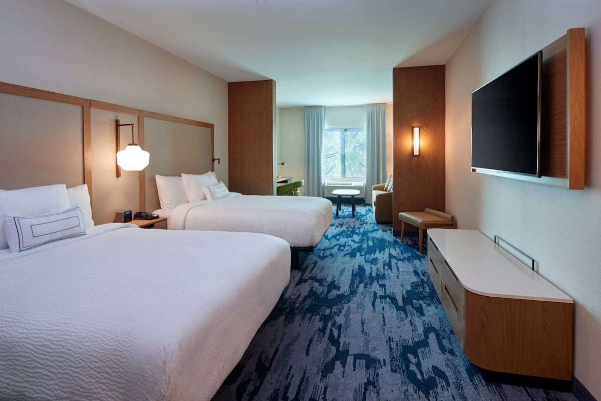 A hotel room with two beds, a desk, a chair, a TV, and a window with curtains.