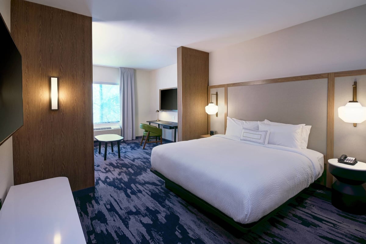 A hotel room with a large bed, a desk, a chair, a TV, and a phone on a side table.