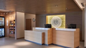Un espace d’accueil comprenant un comptoir de réception en bois, une horloge, un élément décoratif mural et un réfrigérateur pour les boissons.