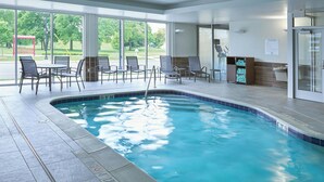 Un espace piscine avec des chaises et une table, un bord de piscine carrelé et une vue sur l’extérieur.
