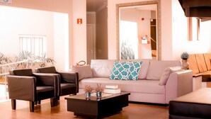 A modern living room with a sofa, two armchairs, and a coffee table. There is a large mirror on the wall and a door leading to another room. - Mirante Hotel (Itapejara d'Oeste)
