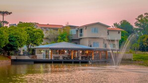 A waterfront restaurant with outdoor seating, a fountain, and a building with multiple stories in the background. - Mirante Hotel (Itapejara d'Oeste)