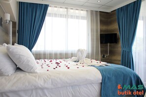 A hotel room with a bed, blue curtains, a TV, and a wall-mounted TV. - Mas Otel (Edremit)