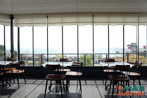 A restaurant with tables and chairs arranged for dining, large windows offering a view of the cityscape, and a modern interior design.