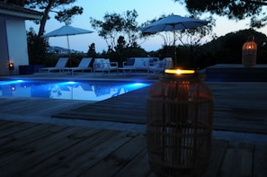 A wooden deck with a pool, lounge chairs, umbrellas, and a lantern. - Les Suites d'Agosta (Albitreccia)