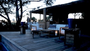 An outdoor deck with a wooden floor, a white sofa, a small table, and a blue chair. - Les Suites d'Agosta (Albitreccia)