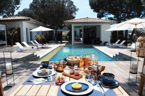A poolside breakfast setup with lounge chairs, a dining table, and a swimming pool. - Les Suites d'Agosta (Albitreccia)
