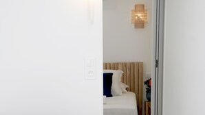 A modern hotel room with a grey sofa, a bed with a wooden headboard, and a small side table with a vase. - Les Suites d'Agosta (Albitreccia)