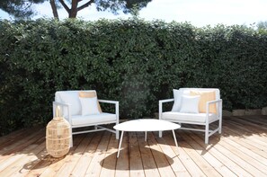An outdoor seating area with two white sofas and a round table, surrounded by a wooden deck and a hedge. - Les Suites d'Agosta (Albitreccia)
