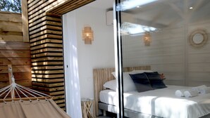 A bedroom with a bed, a small bedside table, and a hanging chair. - Les Suites d'Agosta (Albitreccia)
