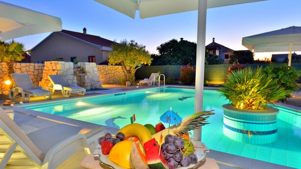 A poolside area with lounge chairs, a fruit bowl, and a stone wall. - Villa Dalmatina Zadar (Zadar)