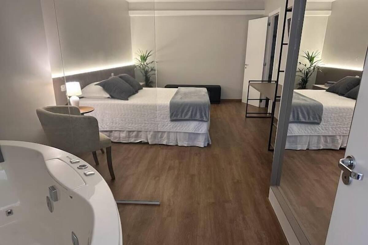 A modern hotel room with two beds, a sitting area with a chair, a small table, and a large bathtub.