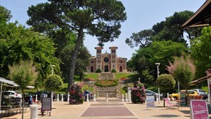 A historic building with a central dome and two towers, surrounded by lush greenery and a paved walkway.