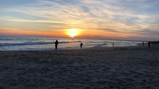 Een strand bij zonsondergang, mensen aan het vissen.