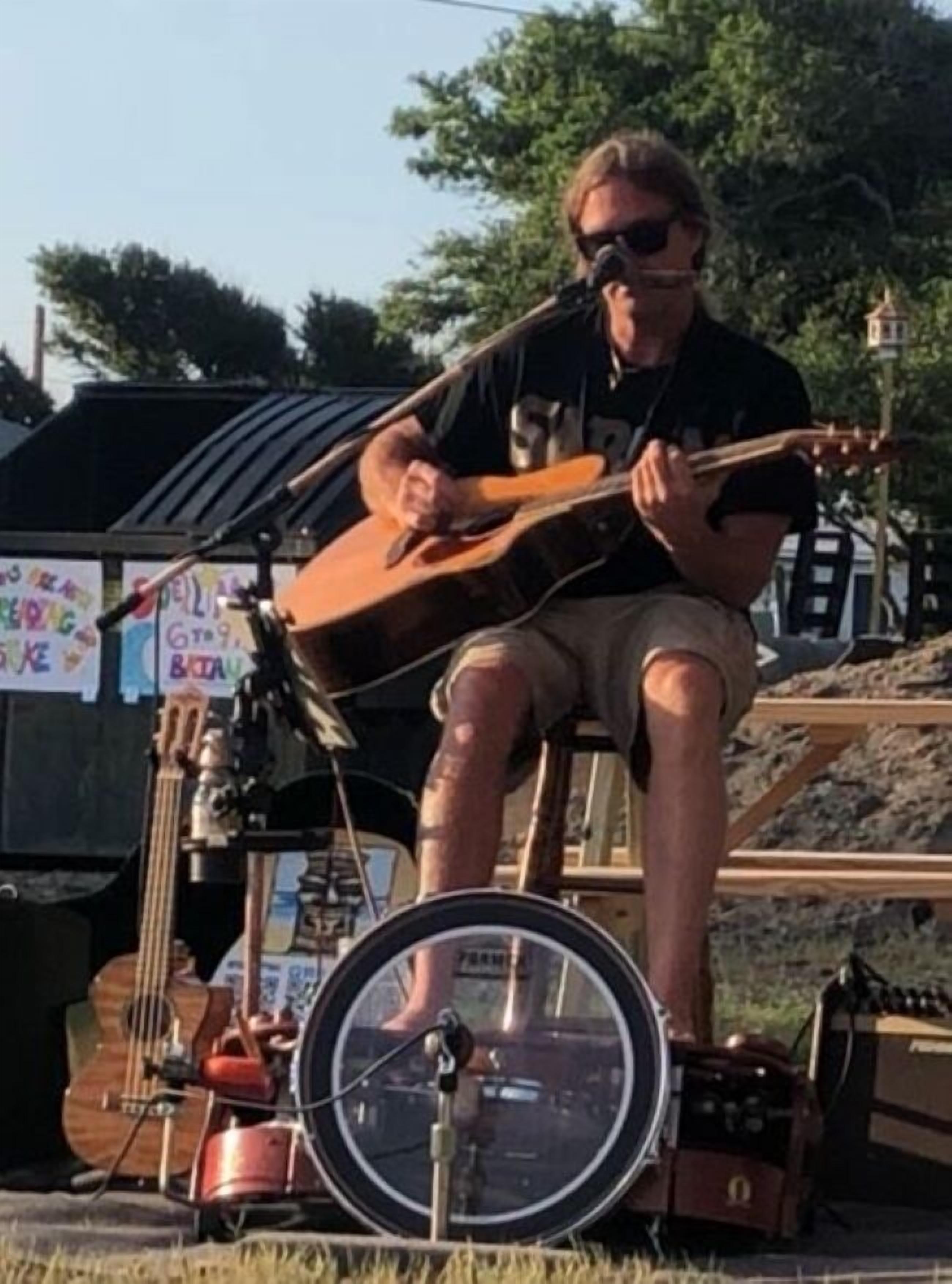 A person playing a guitar on a stage with a microphone and a drum set.
