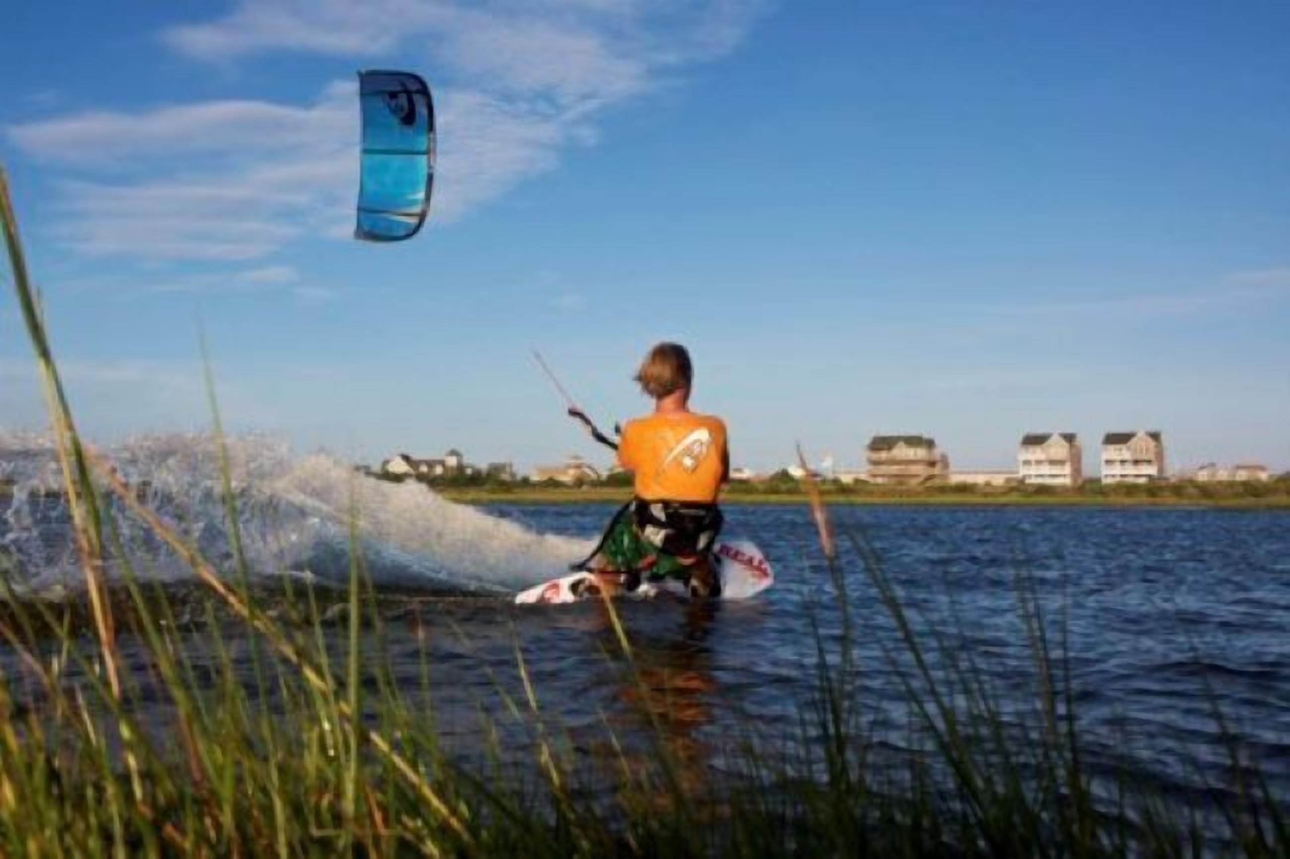 Iemand windsurft op het water, met gebouwen op de achtergrond.