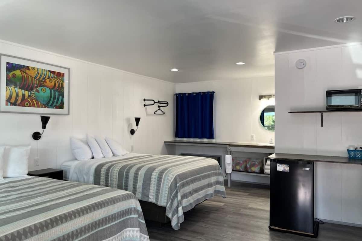 A hotel room with two beds, a kitchenette, a bathroom, and a large window.