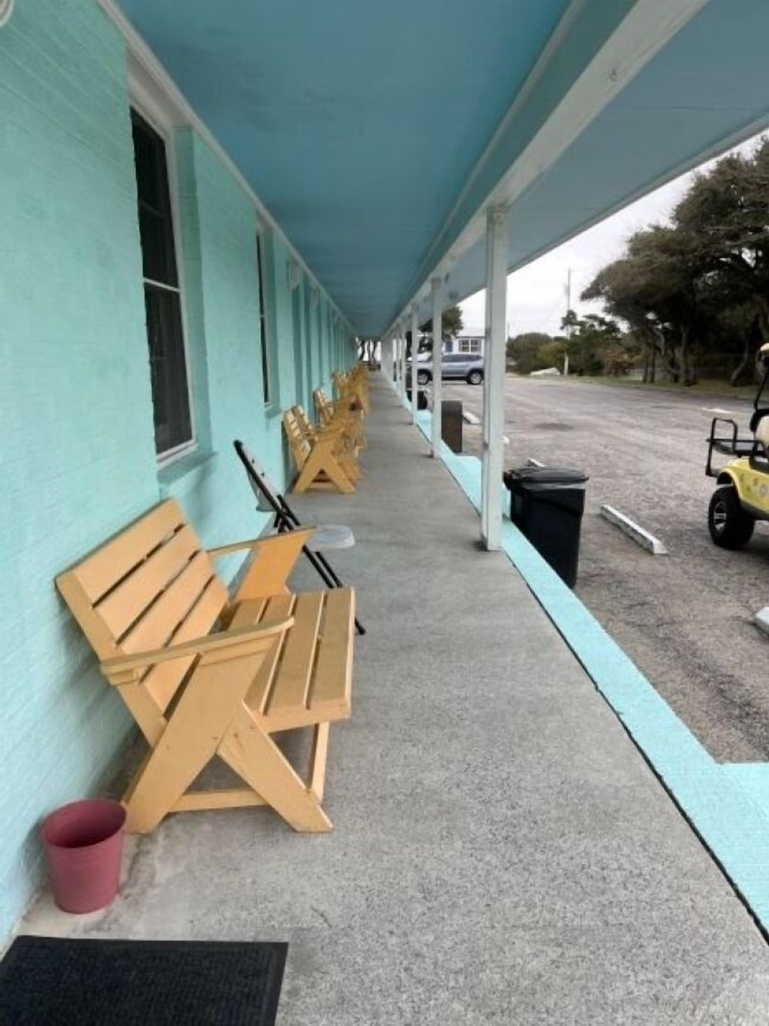 Un motel doté d’une allée couverte, de bancs en bois et d’un chariot de golf garé.