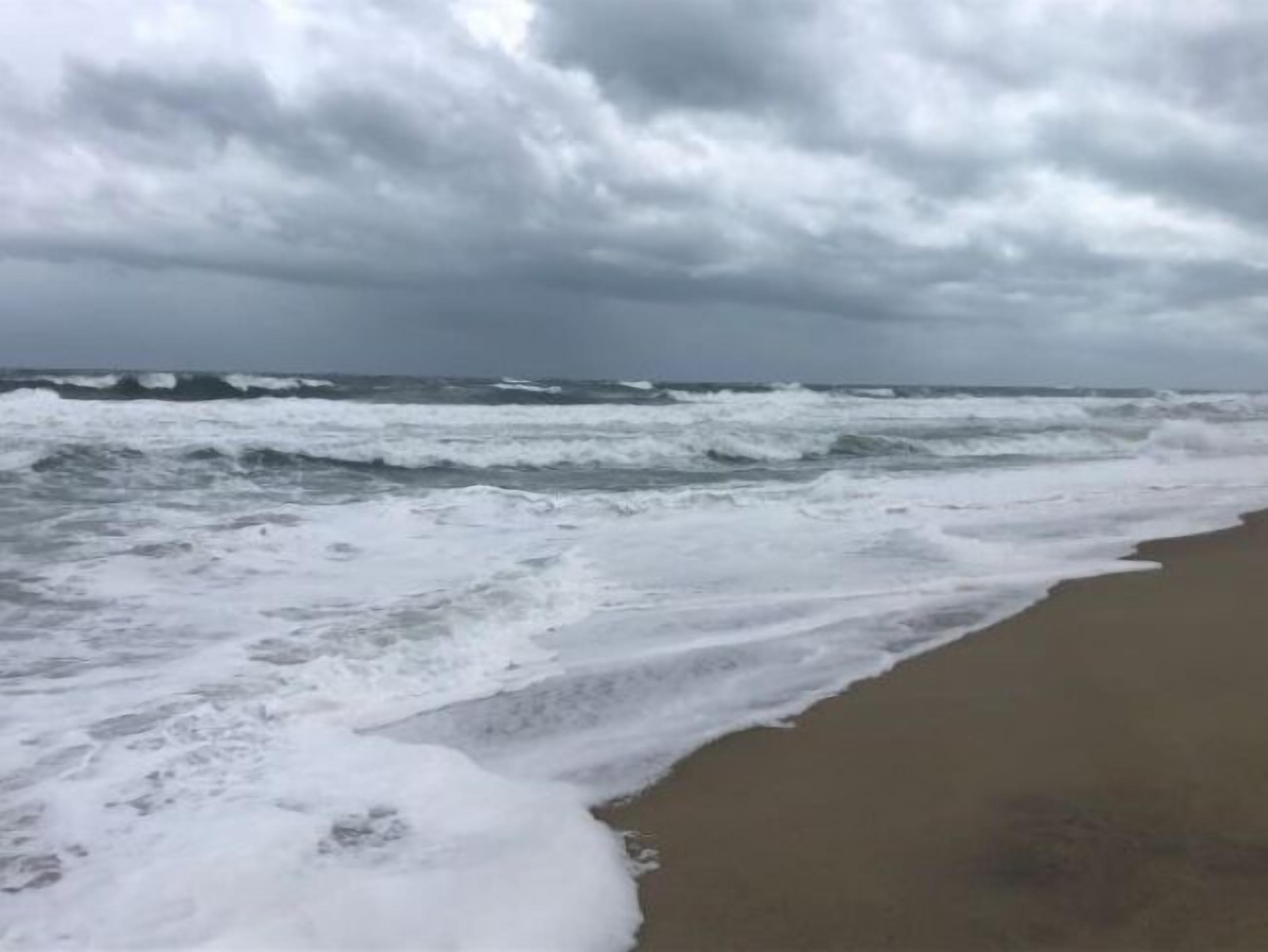 Une plage où les vagues se brisent sur le rivage sous un ciel nuageux.