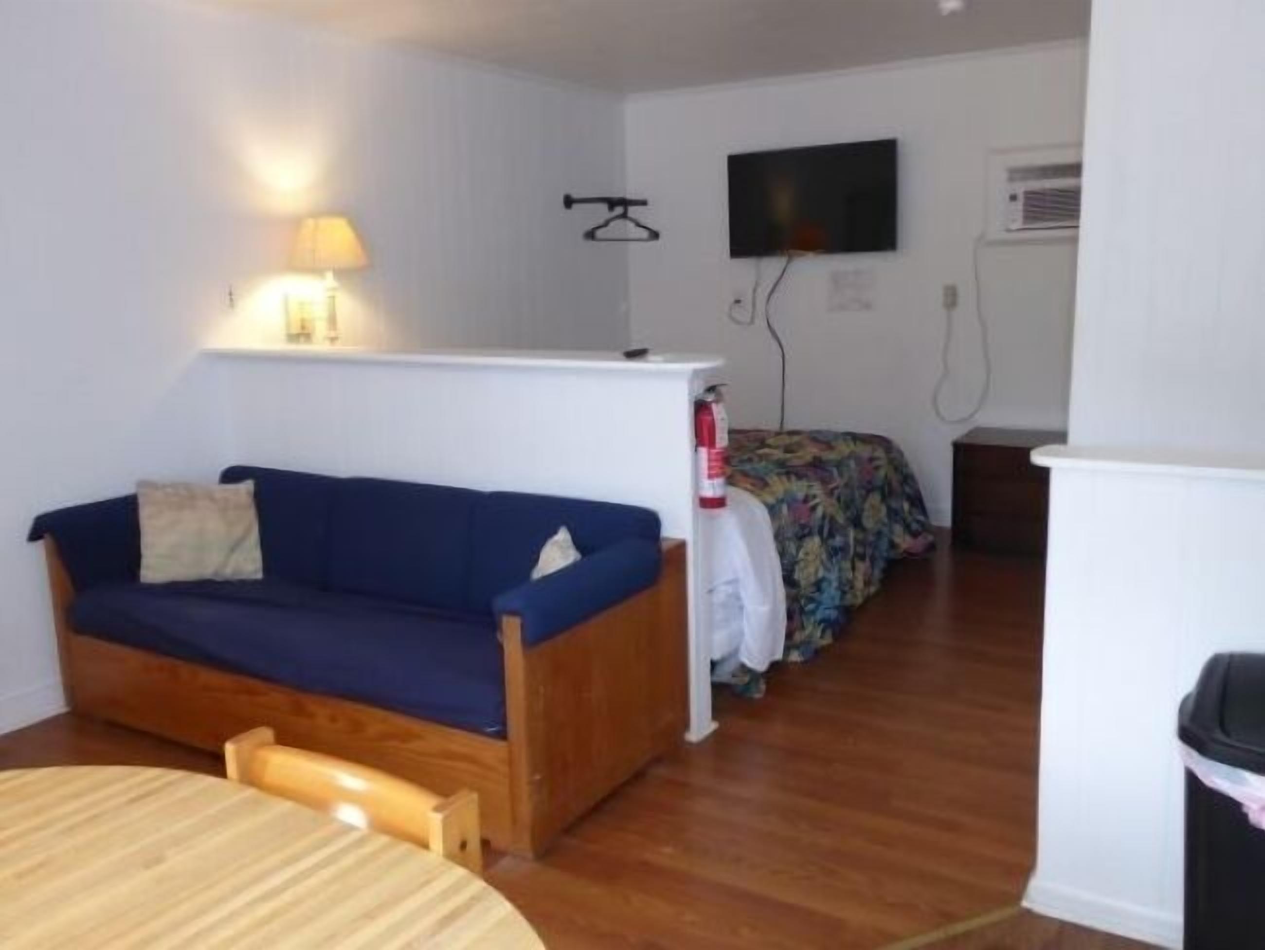 A small, compact room with a wooden sofa, a small table, and a bed with a floral bedspread.