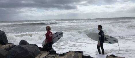 Twee personen met surfboards op het strand, zee in kijkend.