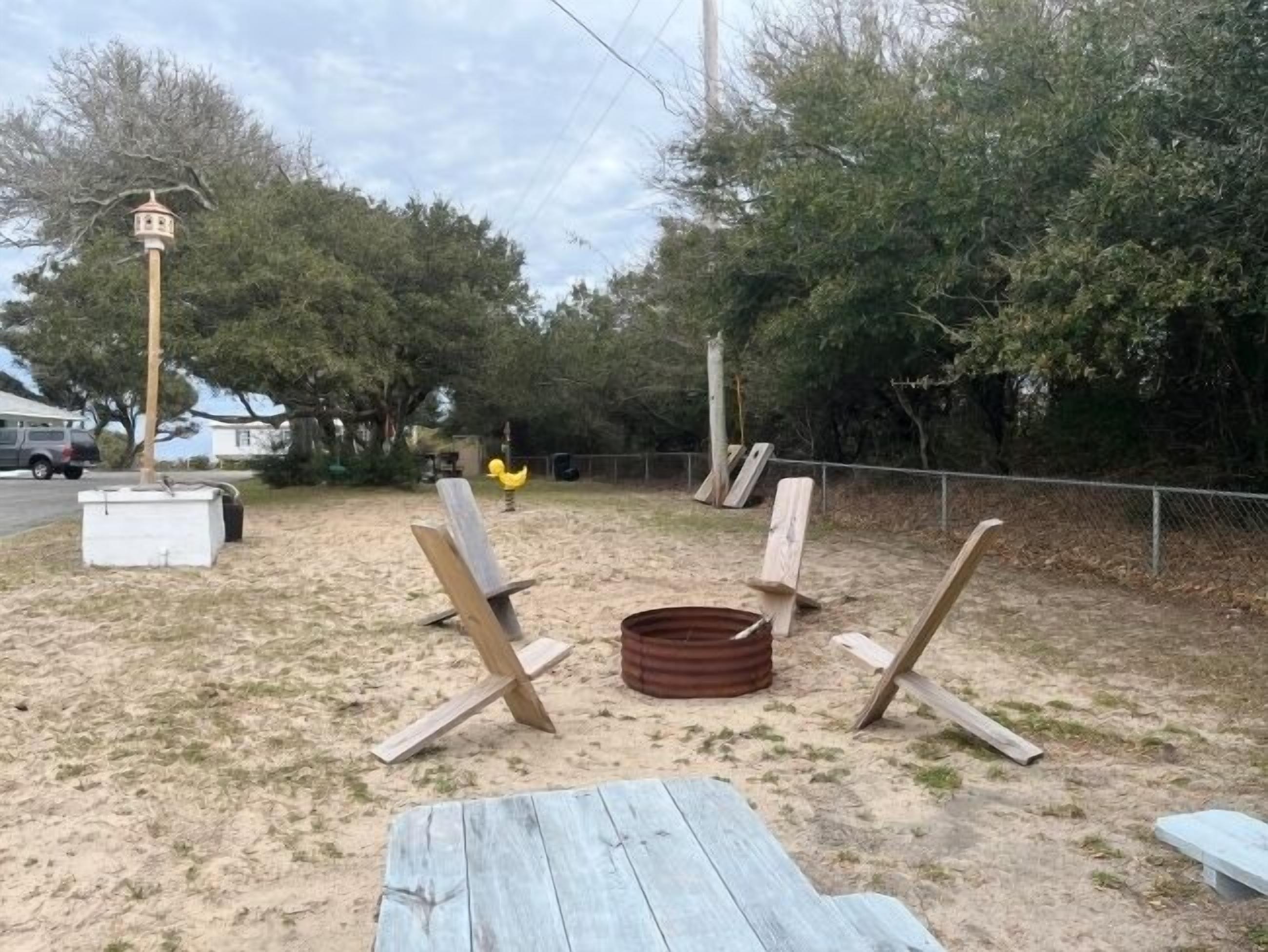 An outdoor seating area with wooden chairs and a picnic table, surrounded by trees and a fence.